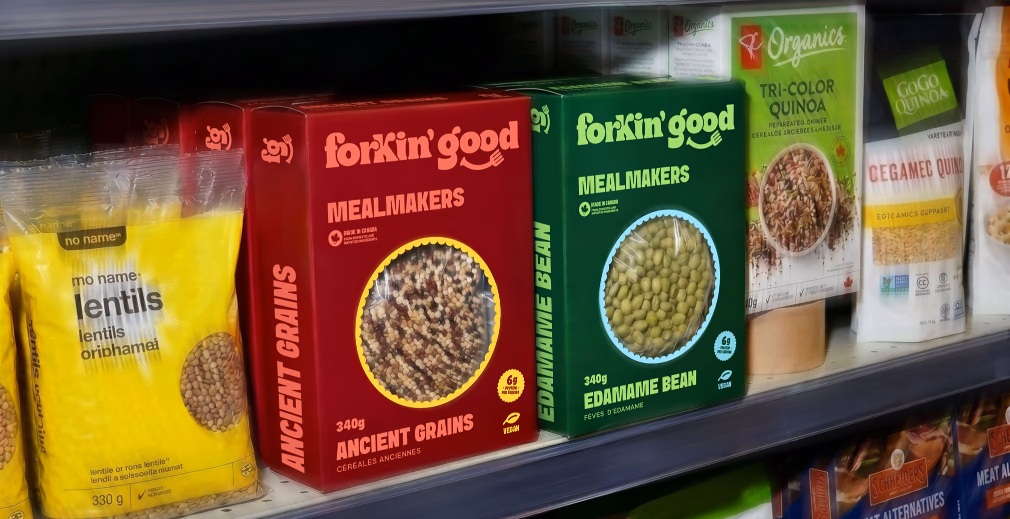 Retail grocery shelf display featuring Forkin’ Good Mealmakers packaging in bold red and green boxes, showcasing ancient grains and edamame beans alongside other organic grain and lentil products in a supermarket aisle.