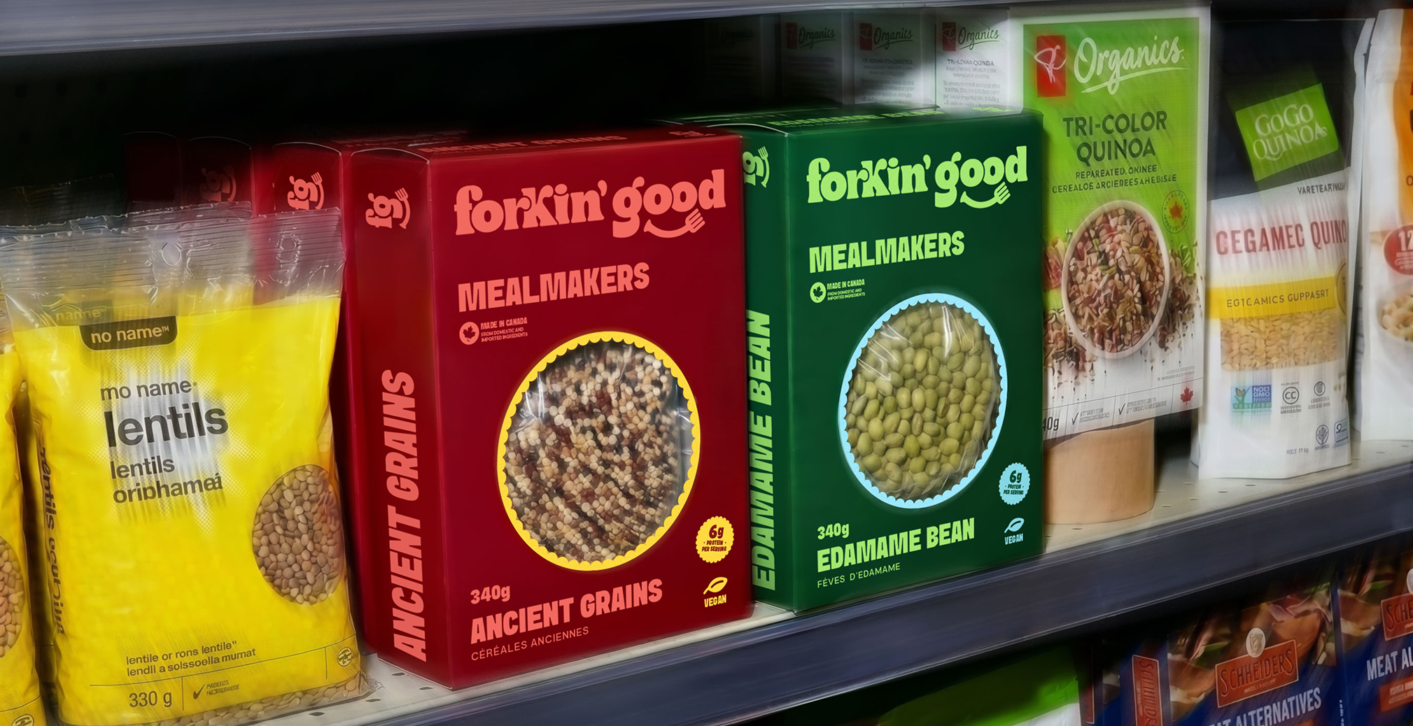 Retail grocery shelf display featuring Forkin’ Good Mealmakers packaging in bold red and green boxes, showcasing ancient grains and edamame beans alongside other organic grain and lentil products in a supermarket aisle.