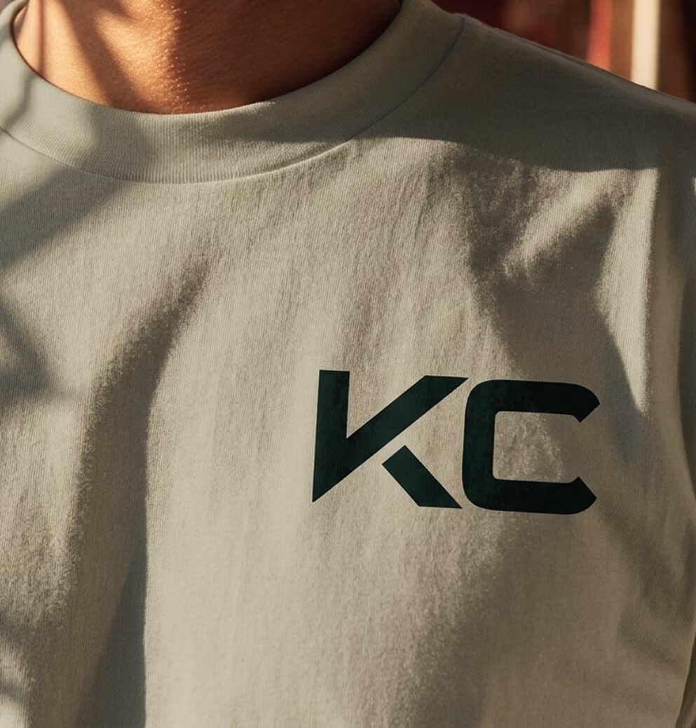Close-up of a cream-colored Koots Canna branded t-shirt with minimalist dark green KC logo detail.