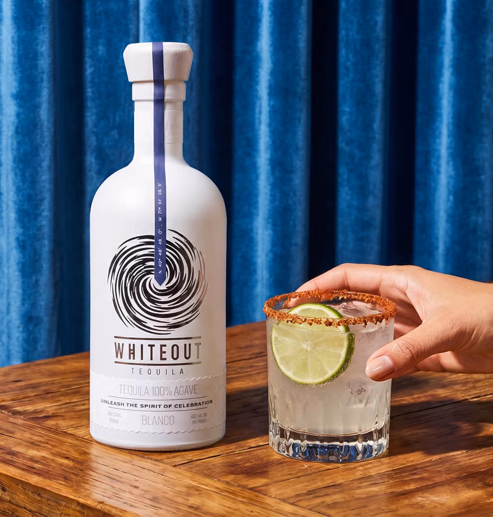 Whiteout Tequila Blanco bottle displayed on a wooden table beside a lime-garnished cocktail, highlighting premium packaging design and elevated tequila branding.