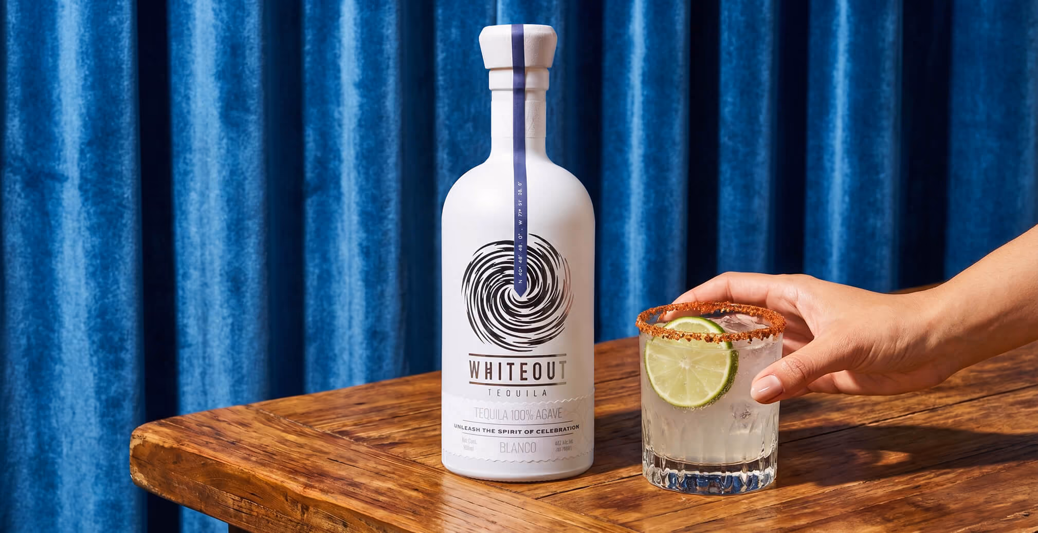 Whiteout Tequila Blanco bottle displayed on a wooden table beside a lime-garnished cocktail, highlighting premium packaging design and elevated tequila branding.