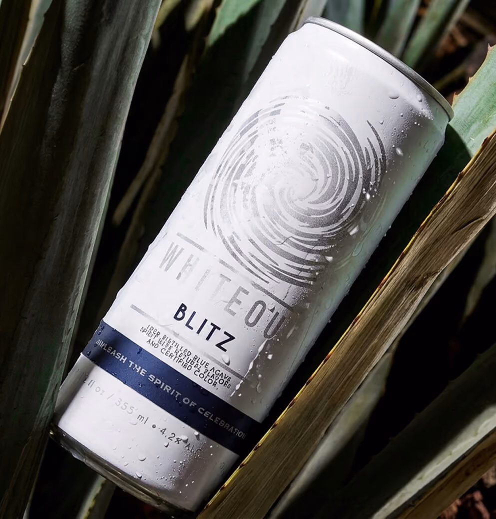 Whiteout Blitz ready-to-drink tequila can nestled among agave leaves with water droplets, emphasizing authentic ingredients and refreshing product appeal.