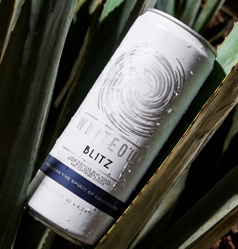 Whiteout Blitz ready-to-drink tequila can nestled among agave leaves with water droplets, emphasizing authentic ingredients and refreshing product appeal.