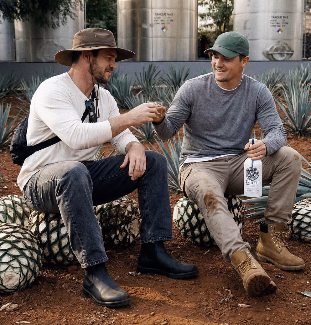Two people sharing tequila in an agave field near production facilities, illustrating authenticity, craftsmanship, and experiential brand storytelling.