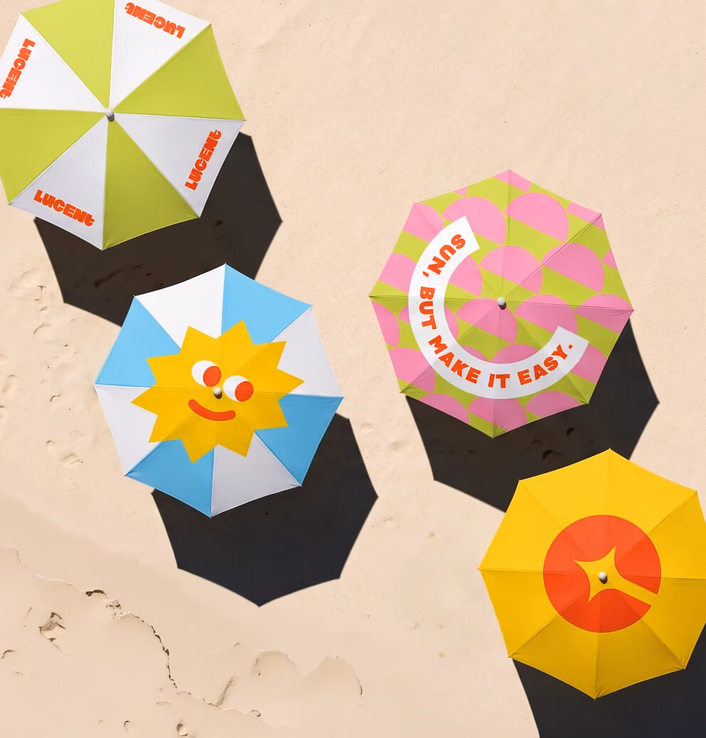 Overhead view of four branded beach umbrellas on sand, displaying Lucent Sun graphics, bright colors, playful patterns, and the smiling sun mascot.