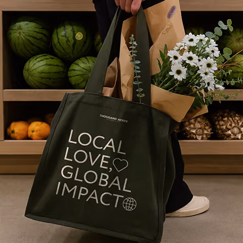 Thousand Acres branded tote filled with groceries and flowers.
