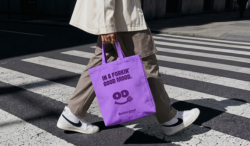 Branded reusable tote bag carried through a city street, illustrating how merchandise extends brand visibility beyond traditional marketing channels.