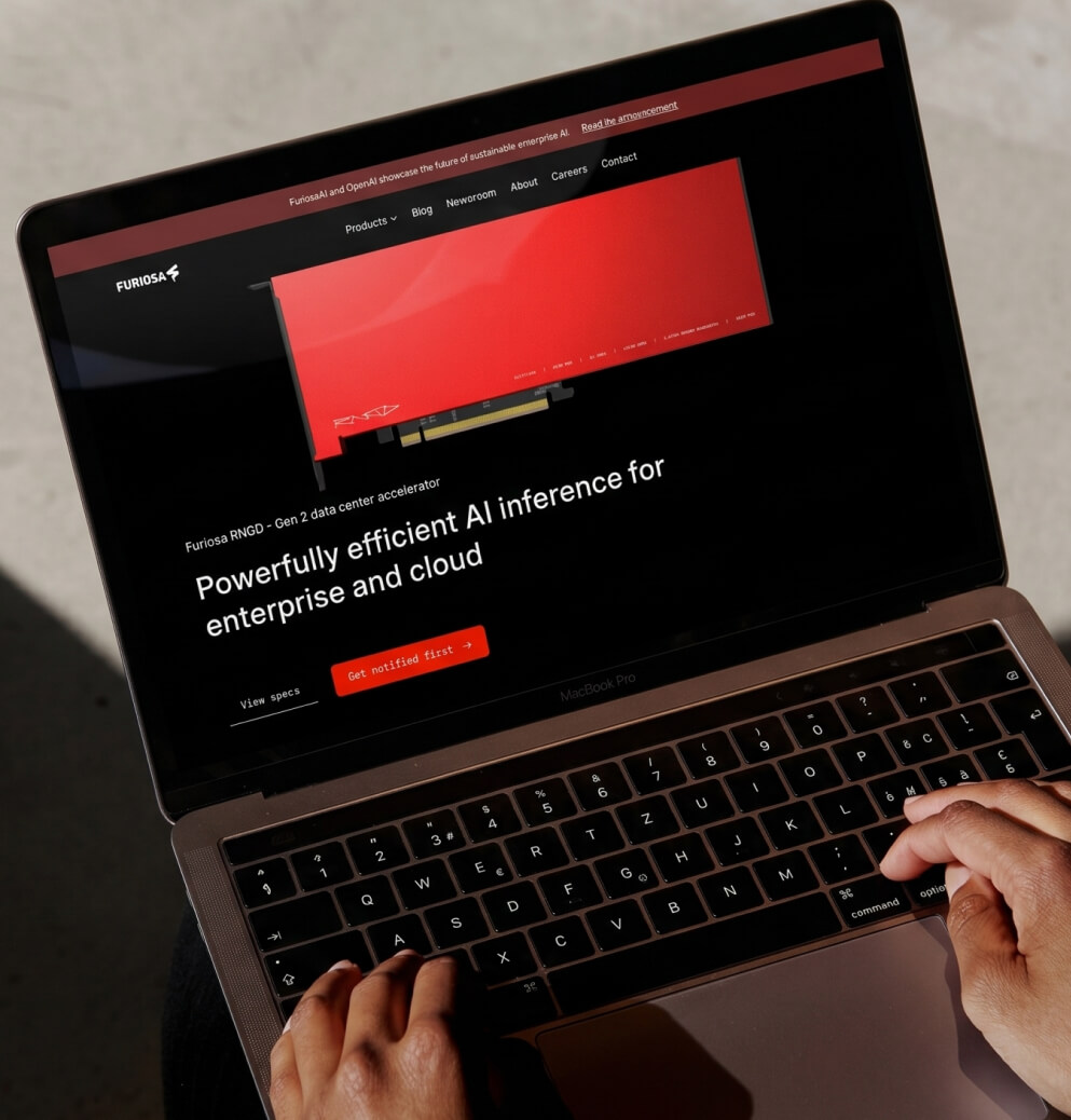 Person using a MacBook Pro to browse the FuriosaAI website, showcasing enterprise AI inference hardware, cloud infrastructure solutions, and high-performance AI accelerator technology.