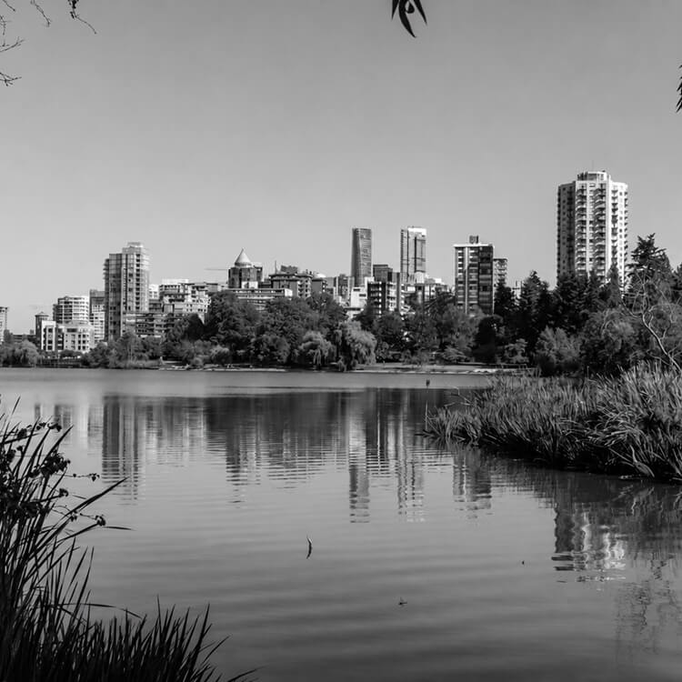 Black and white image of Surrey skyline reflected in a calm lake with surrounding greenery.