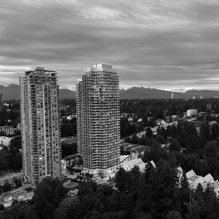 Black and white aerial view of modern residential towers in Surrey with mountains in the background.