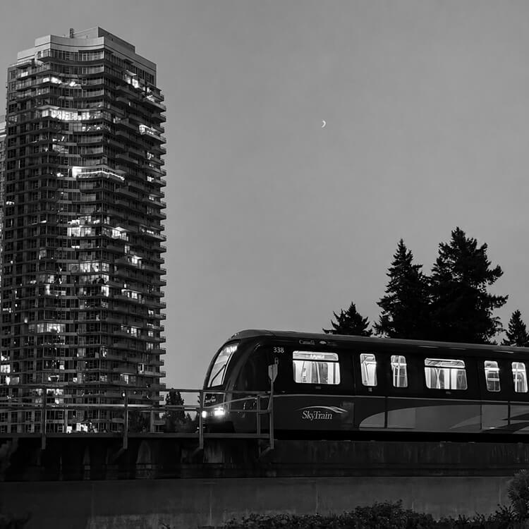Black and white image of a SkyTrain passing through Surrey with high-rise buildings at dusk.