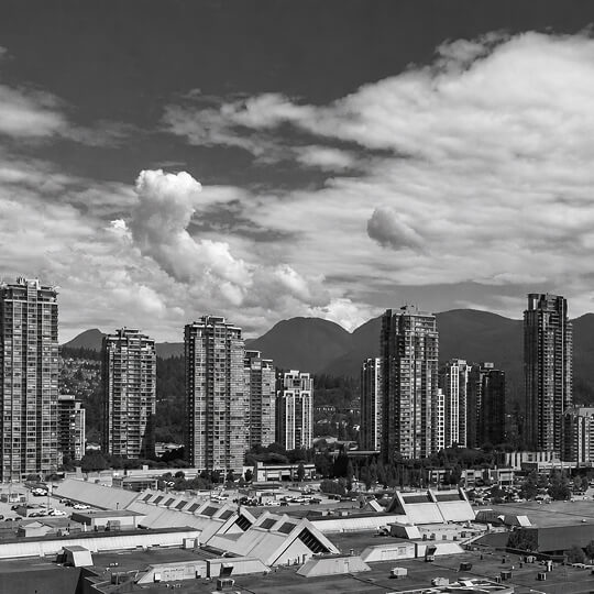 Coquitlam skyline featuring modern residential towers set against the North Shore Mountains under dramatic cloud-filled skies.
