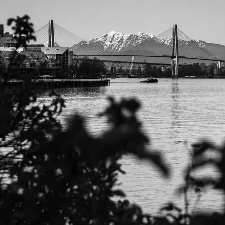 Fraser River view featuring the cable-stayed SkyBridge with snow-capped mountains rising in the background.