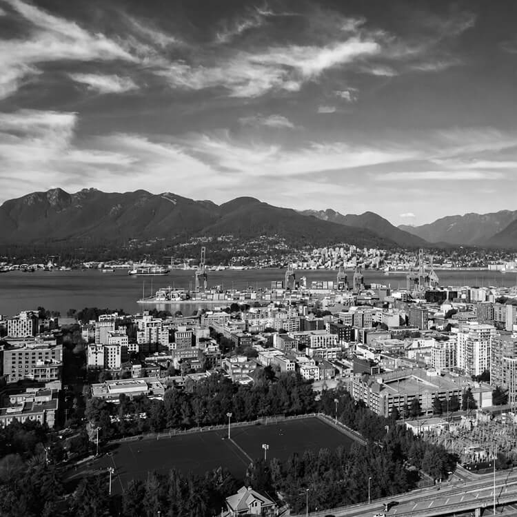 Elevated view across New Westminster toward the Fraser River, industrial waterfront, and surrounding mountain landscape.