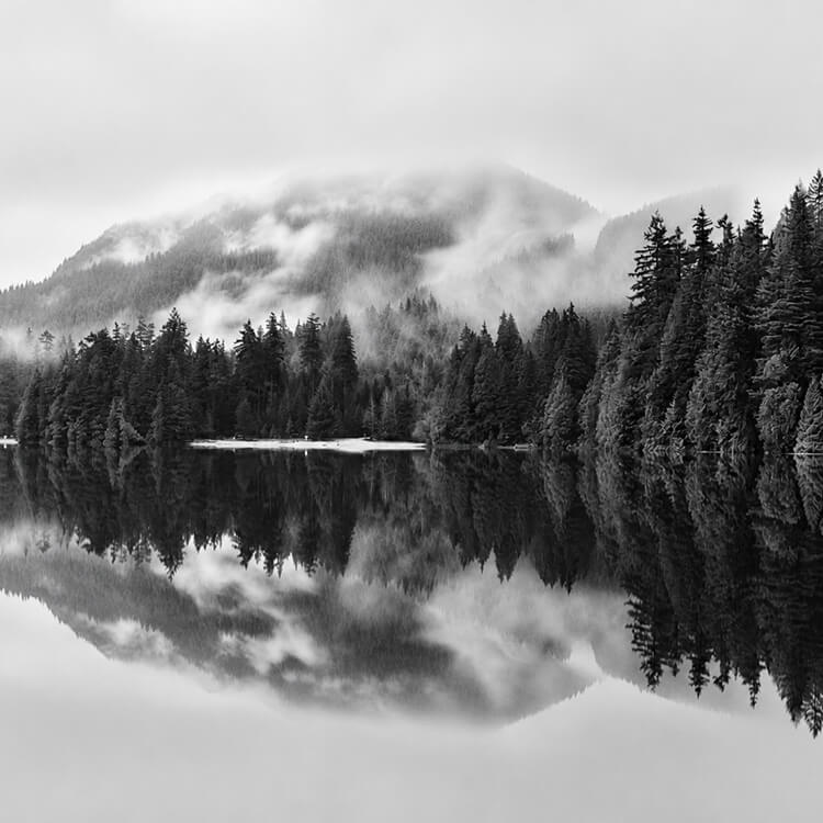 Misty mountain and evergreen forest reflected in the still waters of a lake near Port Moody, British Columbia.