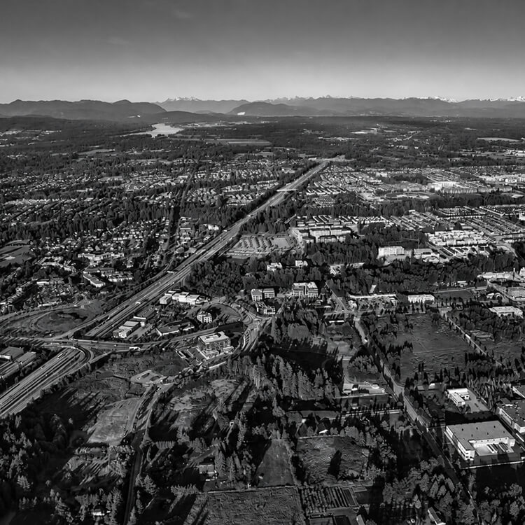 Black-and-white aerial view of Langley showing residential neighborhoods, roads, commercial areas, and mountains in the distance.