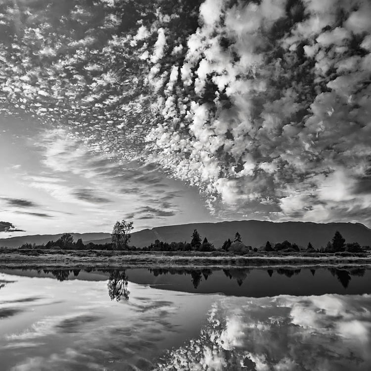 Dramatic cloud formations reflected across calm wetlands with distant mountains near Pitt Meadows, British Columbia.
