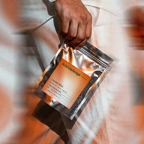 Close-up of a person holding an Acknowledge Cosmic Bliss gummy pouch while wearing white clothing.