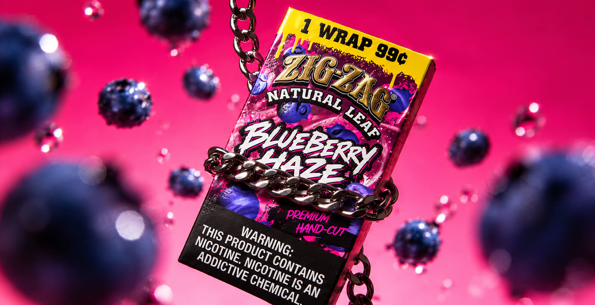 Zig-Zag Natural Leaf Blueberry Haze wrap package wrapped in a metallic chain and surrounded by blueberries against a vivid pink background.
