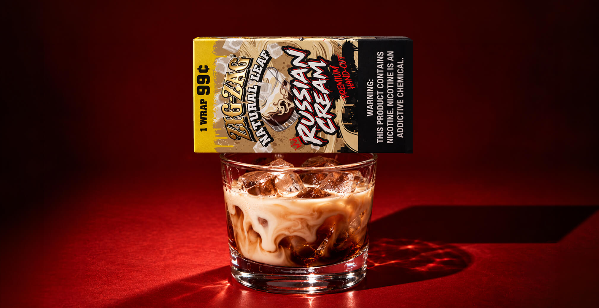 Zig-Zag Natural Leaf Russian Cream wrap package balanced above a glass of iced creamy coffee against a deep red background.