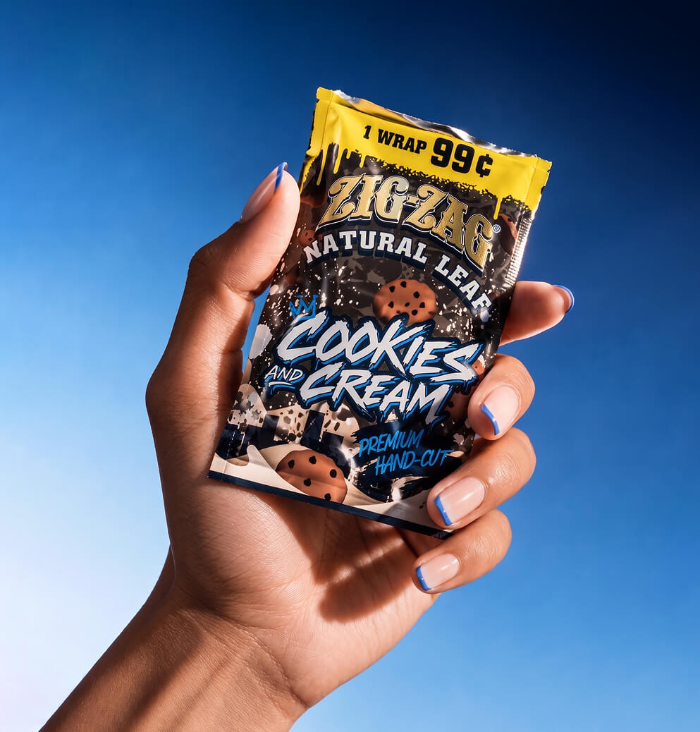 Hand holding a Zig-Zag Natural Leaf Cookies and Cream wrap package against a clear blue background.
