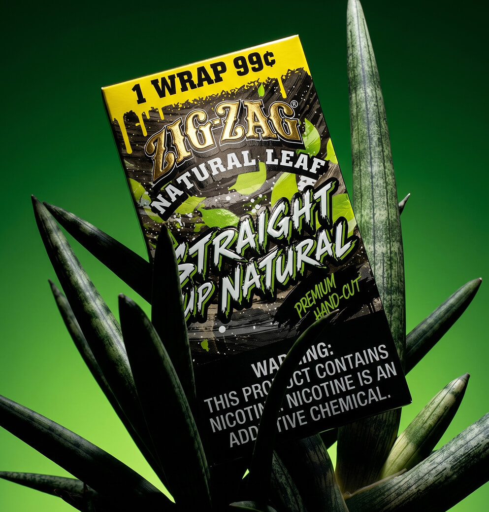 Zig-Zag Natural Leaf Straight Up Natural wrap package positioned among tall green leaves against a vibrant green background.