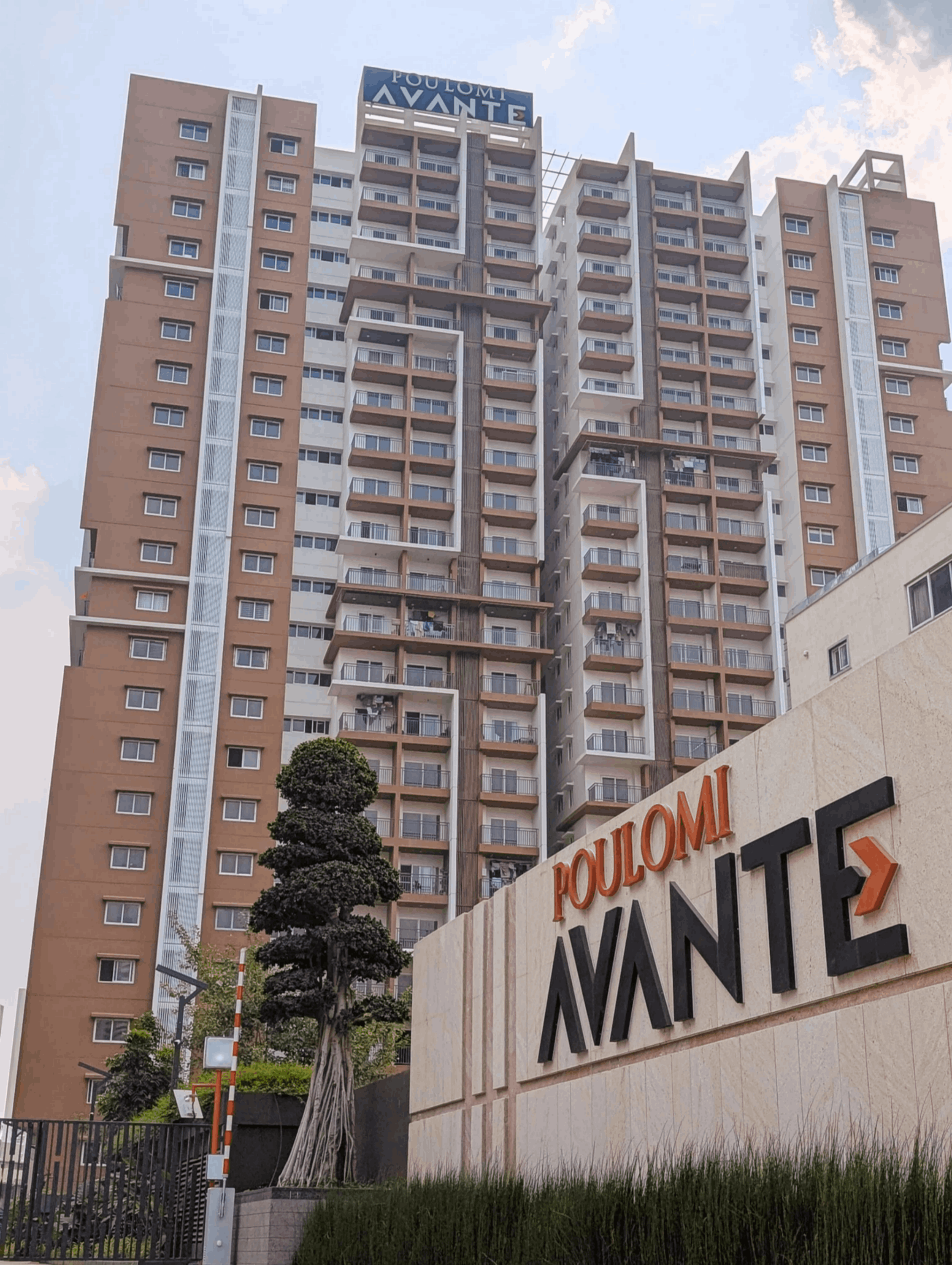 Tall modern apartment building with balconies behind a stone sign reading Poulomi Avante.