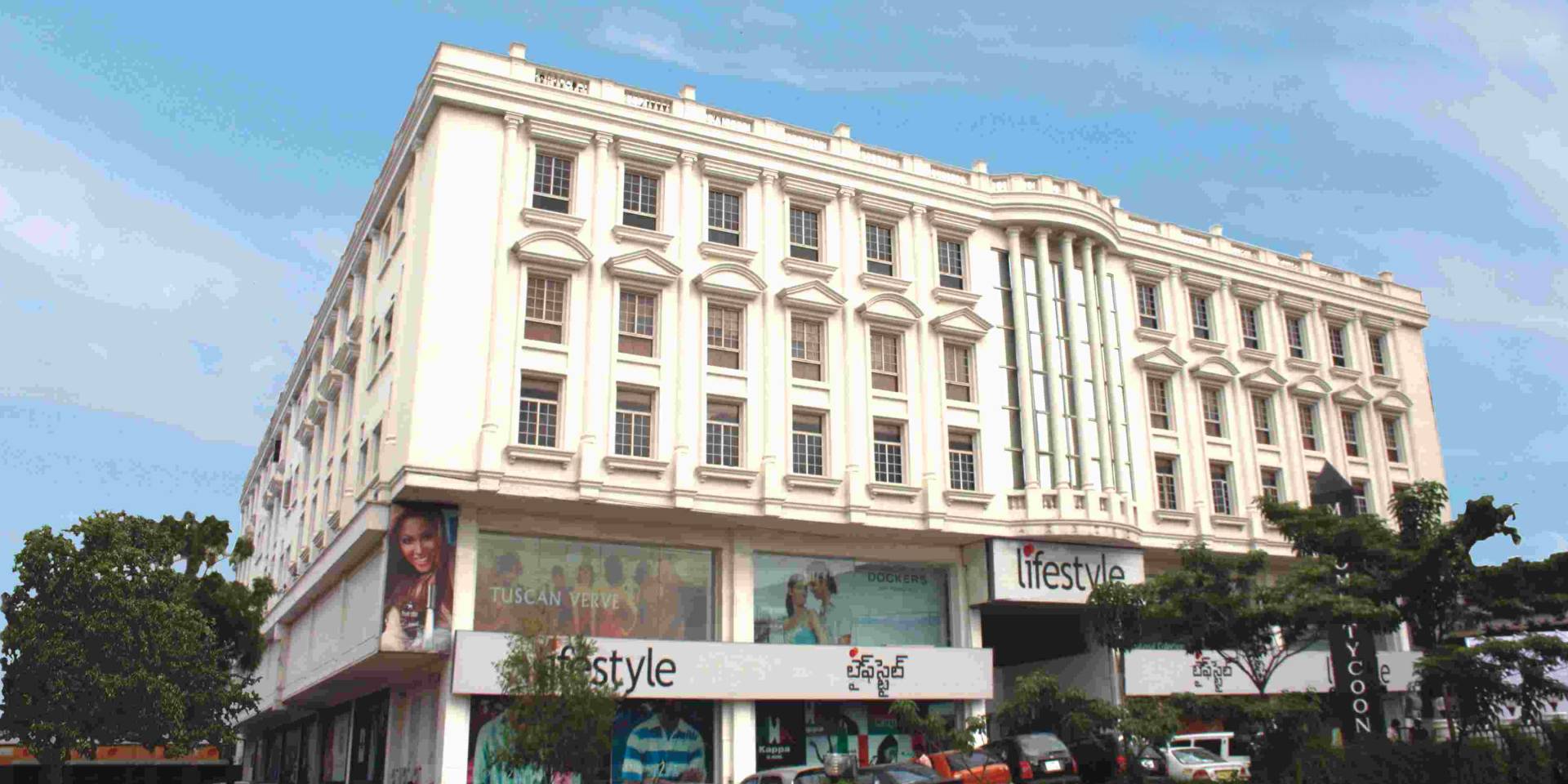 Large white multi-story building with classical columns and windows, housing Lifestyle retail stores at street level.