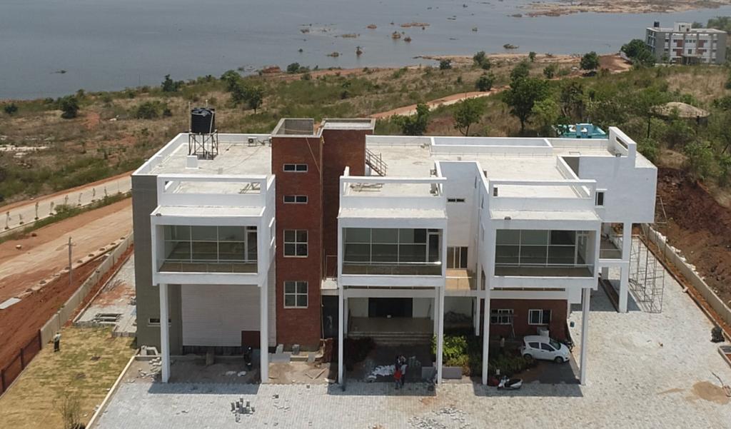 Modern multi-story white and brick building under construction near a reservoir with surrounding undeveloped land.