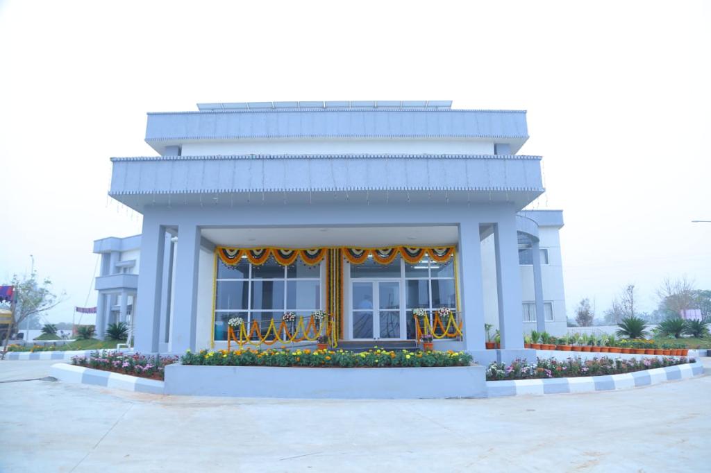 Modern gray building entrance decorated with yellow and orange flower garlands and flower beds in front.