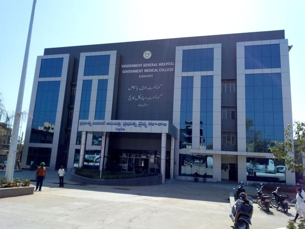 Modern multi-story Government General Hospital and Medical College building with reflective glass windows and people and motorcycles in front.