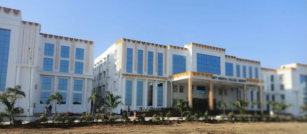 Wide view of a modern government medical college building with large glass windows and landscaped front area under a clear blue sky.