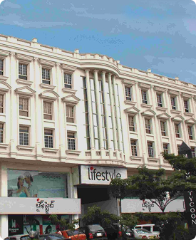 White multi-story commercial building with 'Lifestyle' store sign and cars parked in front under a clear blue sky.