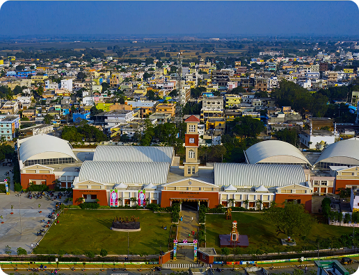 Aerial view of a large clocktower building with curved white roofs in front of a residential cityscape under a clear blue sky.