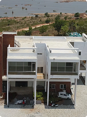 Two modern white townhouses with large glass windows and open garages, set on a cobblestone driveway near a riverbank.