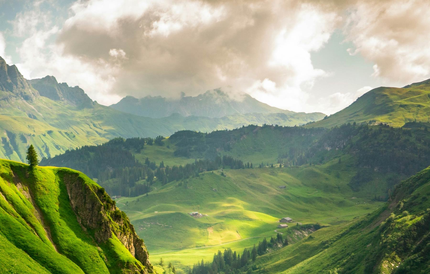 A natural landscape with clouds in the sky above green, natural mountains.
