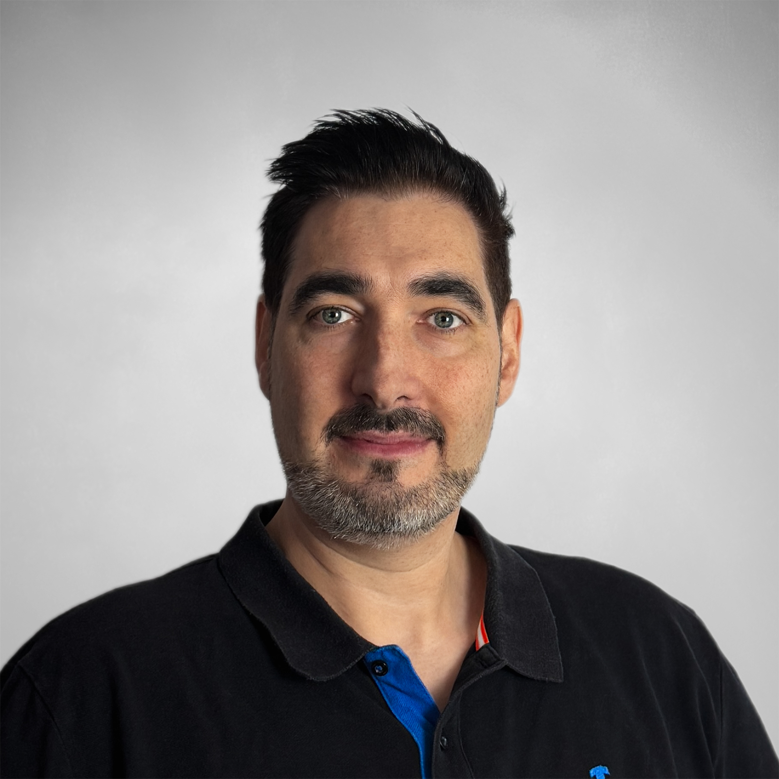 Porträt eines Mannes mit kurzem dunkelbraunem Haar und Bart, der ein schwarzes Polohemd trägt.
