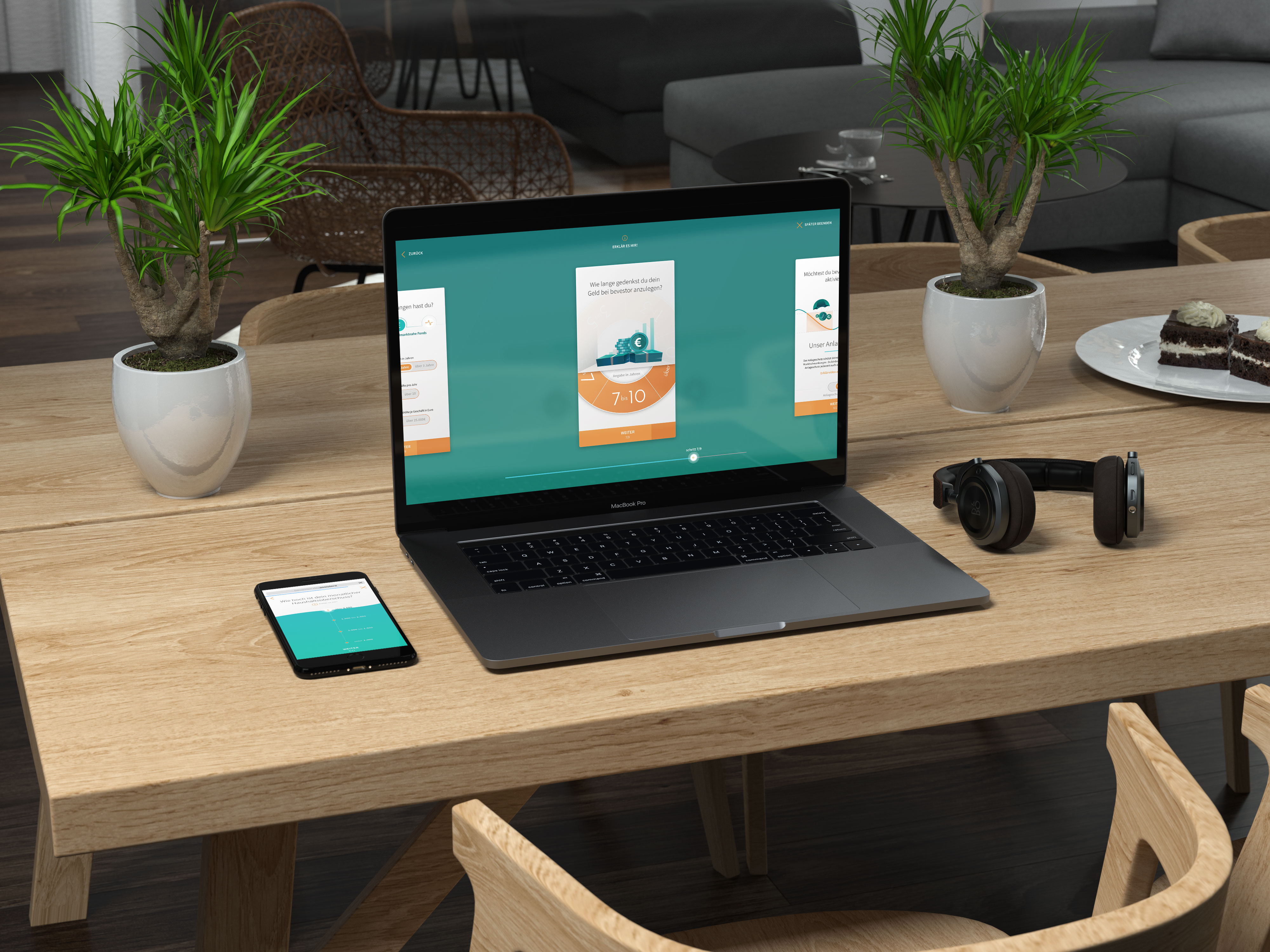 Laptop und Smartphone auf Holztisch zeigen eine Finanz-App, neben zwei grünen Pflanzen, Kopfhörer und Teller mit Kuchenstücken.