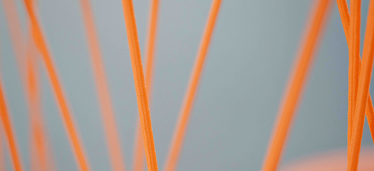 Mehrere orangefarbene, dünne, flexible Schnüre oder Drähte vor einem unscharfen grauen Hintergrund.