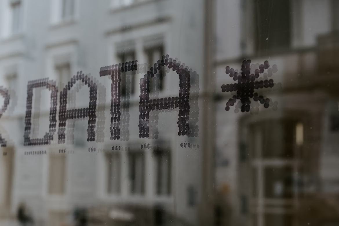 The word 'DATA' spelled out in black dots on a glass window with buildings reflected in the background