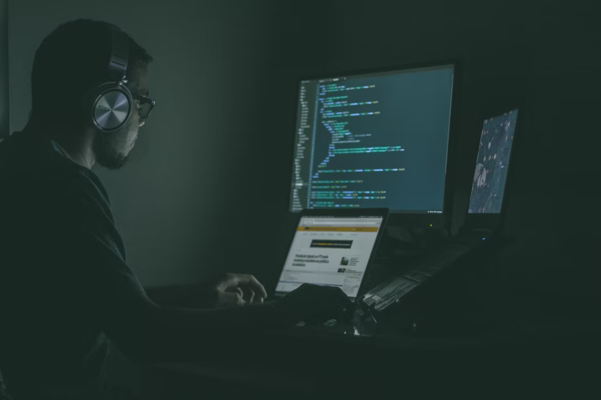 AI security professional working in a dark room with multiple monitors displaying code and cybersecurity content