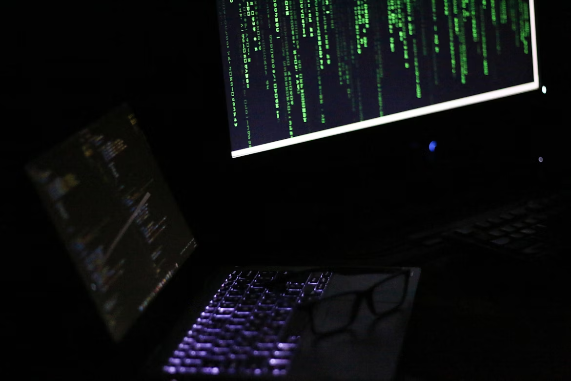 A dark room with two monitors displaying green code on black backgrounds