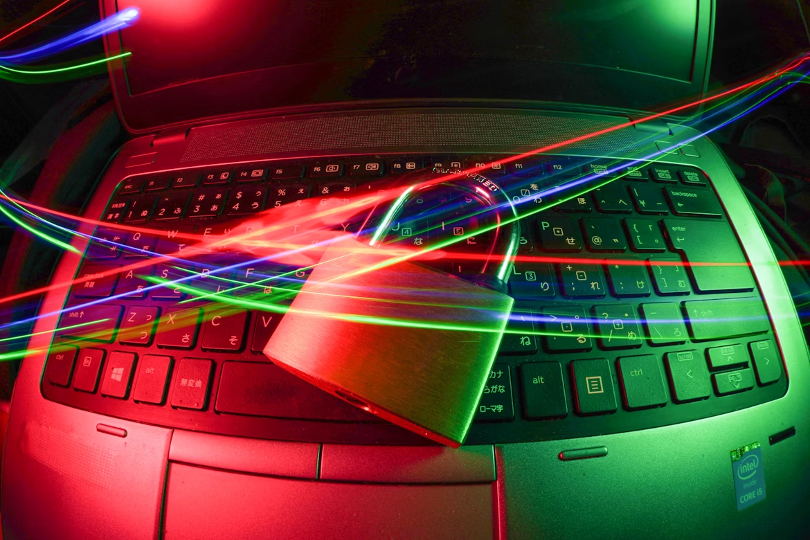 A padlock placed on a laptop keyboard with red, green, and blue light trails representing cybersecurity and protection against digital threats