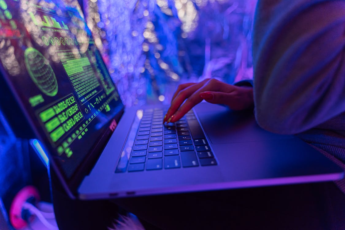 Close-up of a person typing on a laptop with neon green cybersecurity code and system data displayed on the screen, symbolizing AI threat hunting