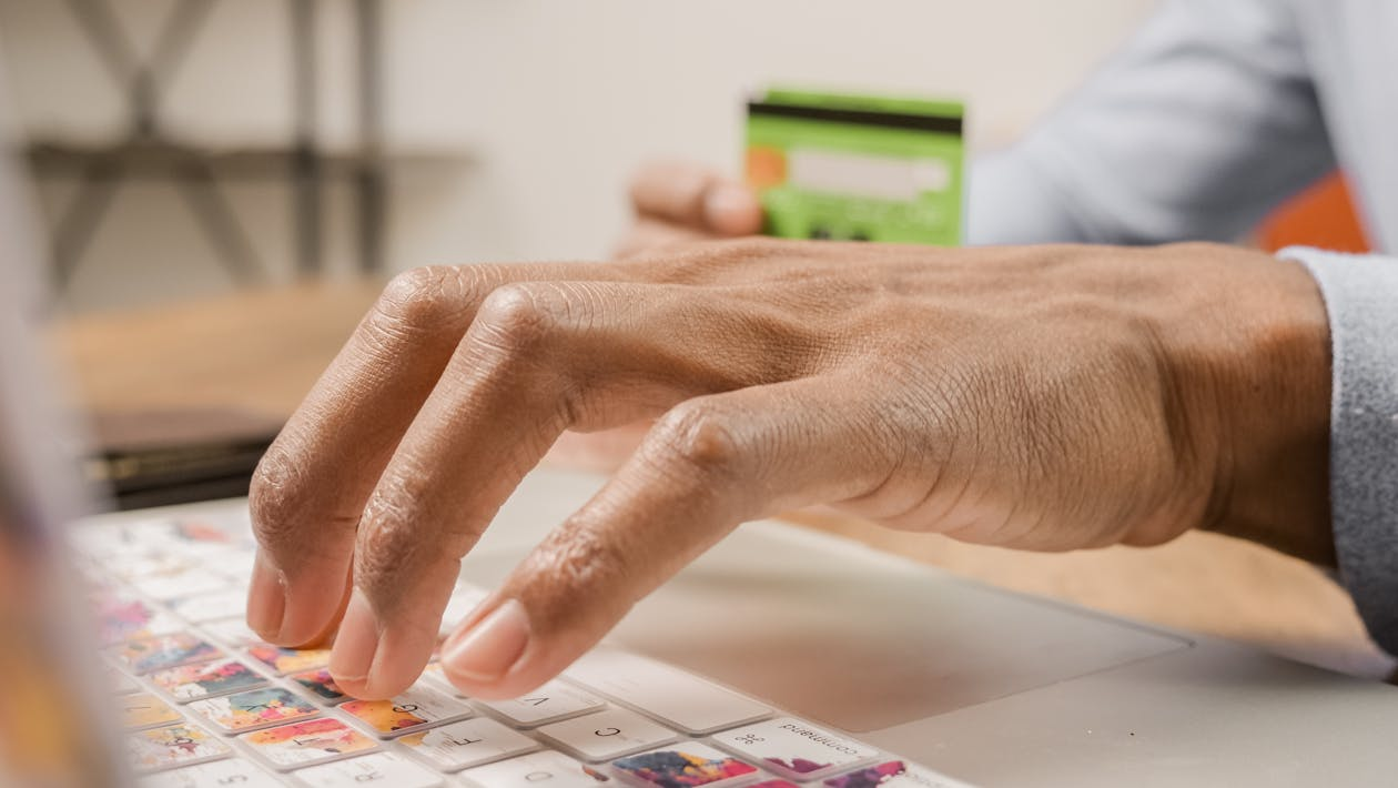 Close-up of a person typing on a laptop keyboard while holding a credit card, symbolizing data security and protection against AI-related cyber risks