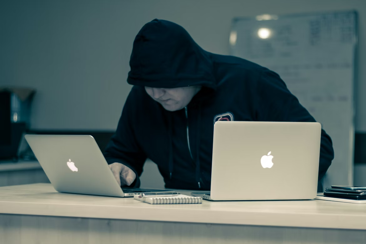 Hooded attacker using laptops to carry out a data poisoning attack against an AI system