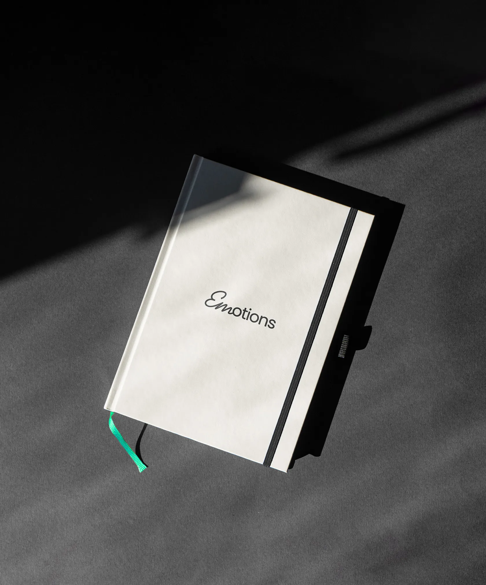 Un carnet de notes avec une couverture blanche et noire, portant le mot 'Emotions' sur la couverture, posé sur une surface grise.