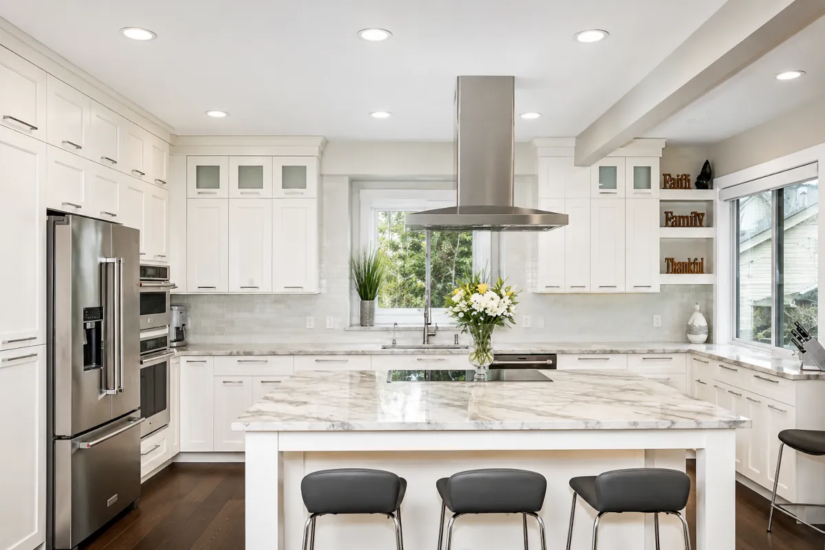 White shaker kitchen remodel with a marble-topped island, stainless island range hood, and dark hardwood flooring
