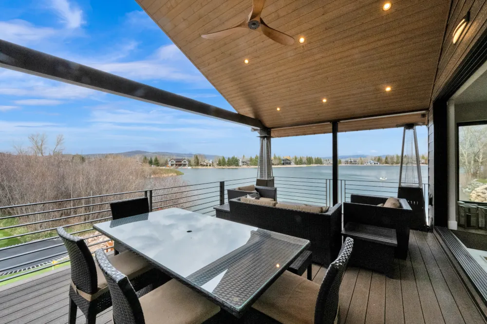 Covered lakefront deck with a wood-paneled ceiling, cable railing, and outdoor dining and lounge seating