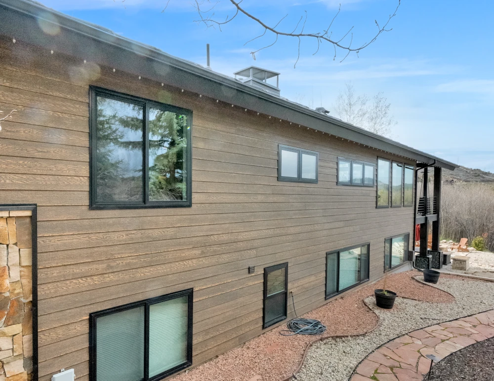 Two-story home exterior with horizontal wood-look siding, black-framed windows, and stone accent columns